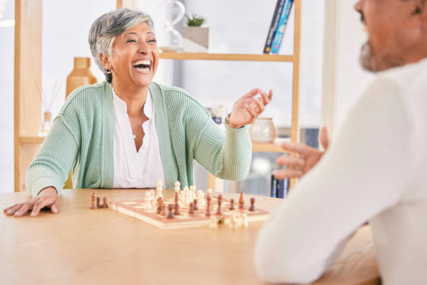 lachendes, spiel und älteres paar mit schach in einem haus im ruhestand für einen wettbewerb. glücklich, zusammen und ein lustiger und älterer mann und eine ältere frau mit einem brett für eine herausforderung oder eine bindung zu gesprächen - senior couple couple partnership discussion stock-fotos und bilder