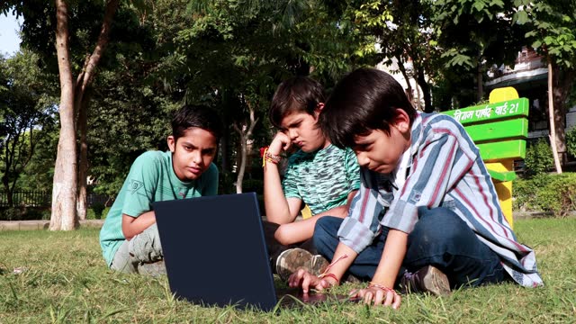 Children using laptop outdoor in the park and playing with rubics cube