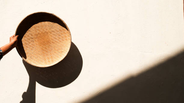 A male hand holding a bamboo tray against a background of shadows from sunlight