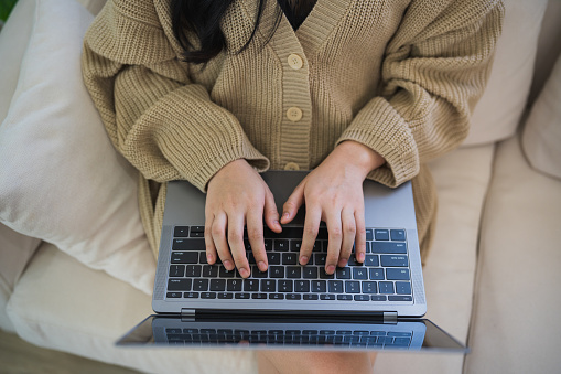 Top view. Asian freelance woman smile lying relax and typing on keyboard and working on laptop on sofa couch. Entrepreneur woman working for her business at living room home. Business work home.