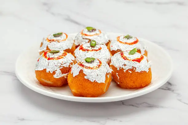 Close-up of an Indian Sweet "Motichoor Ladoo" also Called Boondi Ladoo in white ceramic plate. Isolated on a Marble background. Front view.