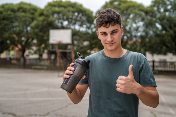 1人の若い白人男性ティーンエイジャーホールドサプリメントシェーカースタンド屋外 - basketball teenager nature outdoors ストックフォトと画像