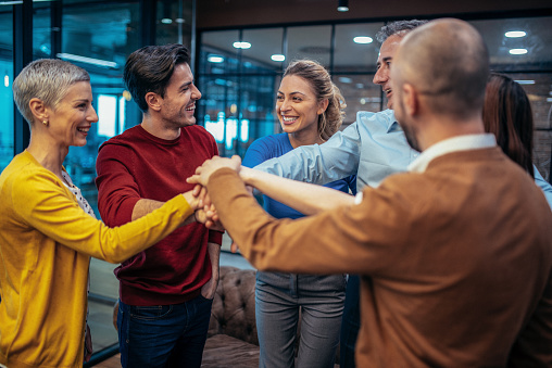 Photo of international business team showing unity with putting their hands together on top of each other. Concept of teamwork. Smiling business persons stacking hands.