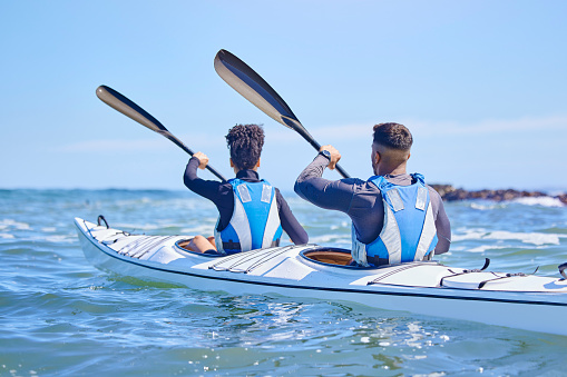 Water, man and woman in kayak and sports on lake, beach or river for exercise together on vacation. Ocean holiday, adventure and fitness, couple in canoe for training workout in teamwork on blue sky.