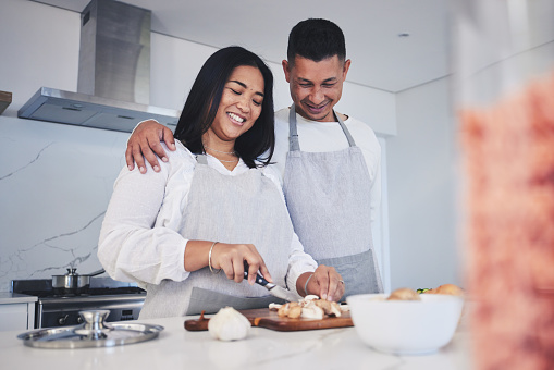 Hug, cooking and love with couple in kitchen for food, health and lunch recipe. Happy, nutrition and dinner with man and woman cutting vegetables at home for diet, wellness and romance together