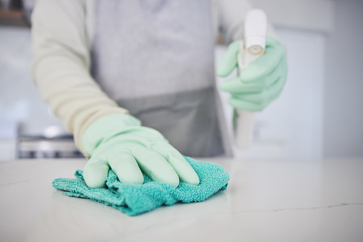 Person, hands and cleaning table with spray bottle in kitchen hygiene, germ or bacteria removal at home. Closeup of maid or cleaner wiping counter with cloth and detergent in healthy disinfection