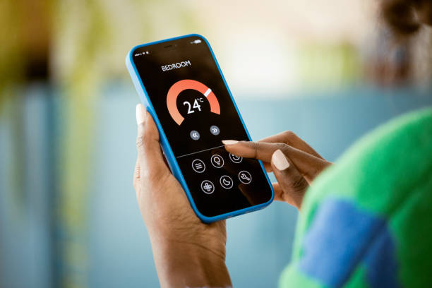 Woman using mobile phone to control termostat at home Afro american woman using smart phone with smart home application. Close up of hands, unrecognizable person. smart thermostat stock pictures, royalty-free photos & images