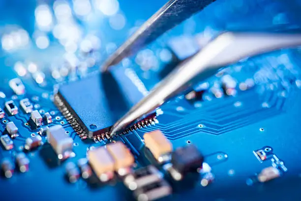 Photo of Electronic technician holding tweezers and assemblin a circuit board.