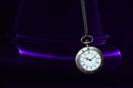 Hypnosis session. Vintage pocket watch with chain swinging over surface on dark background among faded clock faces, magic motion effect