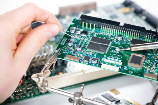 Electronic technician holding tin wire and soldering elements on circuit board. 