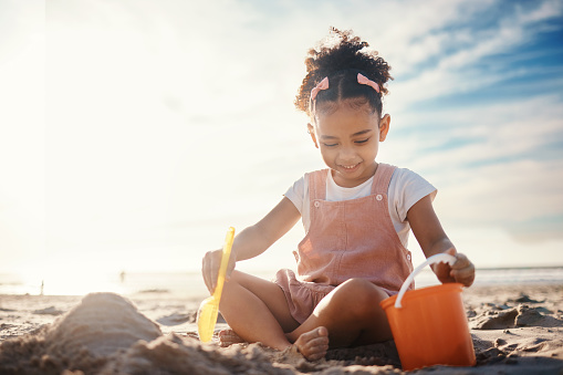 Sand, castle and girl kid at beach for fun games, freedom and summer holiday with mockup sky. Happy child, bucket and building with play toys at sea for development, vacation and relax in sunshine