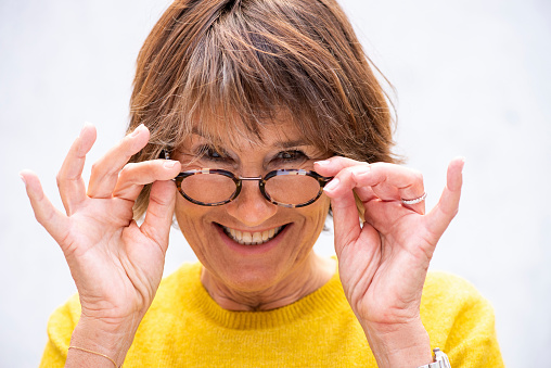 Portrait of happy mature woman removing glasses and peeking