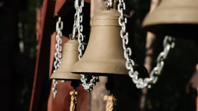 Close up metallic bells hanging in a row outdoors. Changing focus from foreground to background.