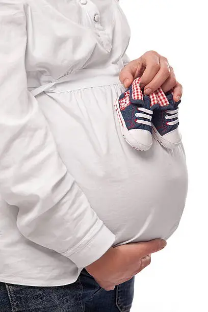 Pregnant woman keeping baby-shoes. Close up shot of belly and shoes.