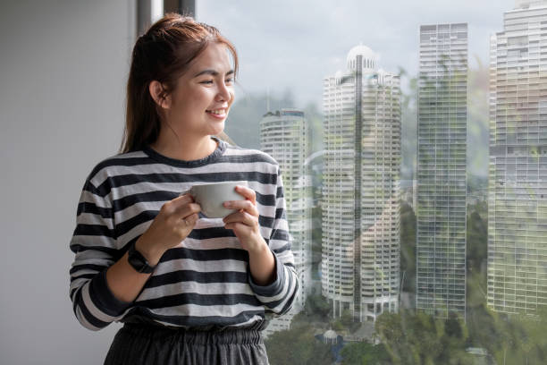 retrato de bela jovem mulher com uma xícara de café e usando fones de ouvido em pé relaxado e feliz. - room service audio - fotografias e filmes do acervo