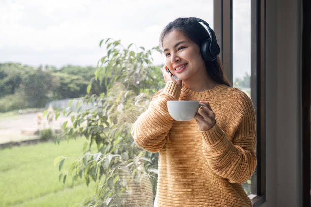 портрет красивой молодой женщины с чашкой кофе и в наушниках, стоящей расслабленной и счастливой. - room service audio стоковые фото и изображения
