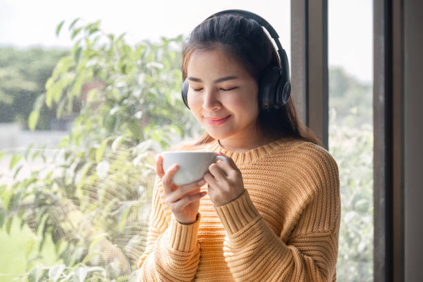 retrato de bela jovem mulher com uma xícara de café e usando fones de ouvido em pé relaxado e feliz. - room service audio - fotografias e filmes do acervo