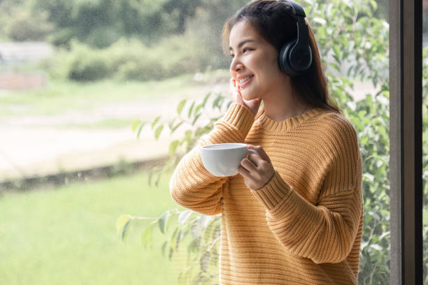 retrato de bela jovem mulher com uma xícara de café e usando fones de ouvido em pé relaxado e feliz. - room service audio - fotografias e filmes do acervo