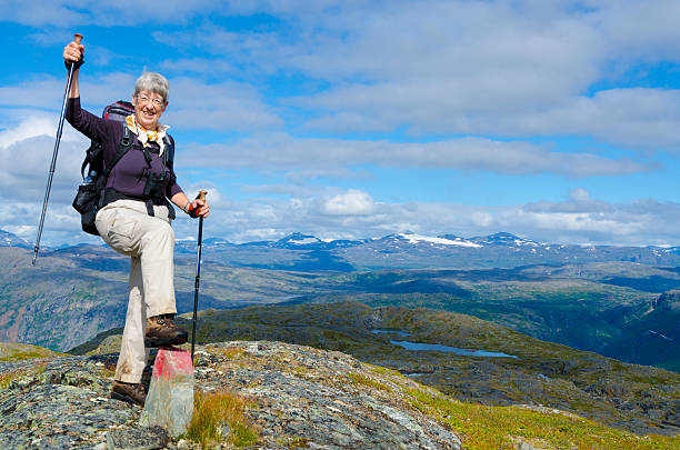 Mature female hiker with backpack, overlooking mountain landscape stock photo