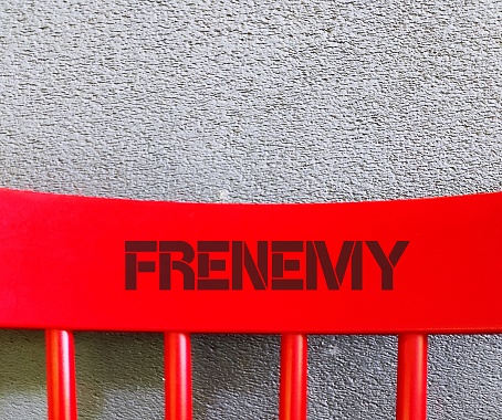 Red chair back on copy space concrete wall with text - FRENEMY - person who combines the characteristics of friend and enemy, rival pretends to be a friend