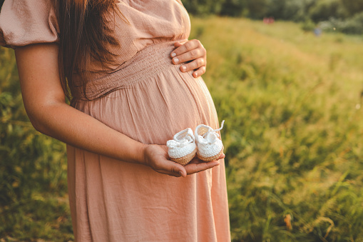 A pregnant woman holds cute baby shoes in her hands, the concept of expecting a baby.