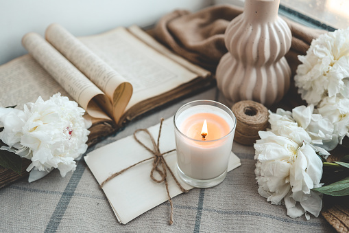Burning candle and white peonies, vintage aesthetic.