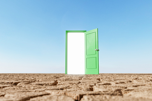 open green door with a bright light coming out of it over a desertic terrain with clear sky. concept of drought, entrance to environmentalism and climate change. 3d rendering