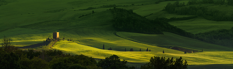 Italian landscape with green meadows and an old fortress tower. Beautiful green field and soft sunlight at sunset