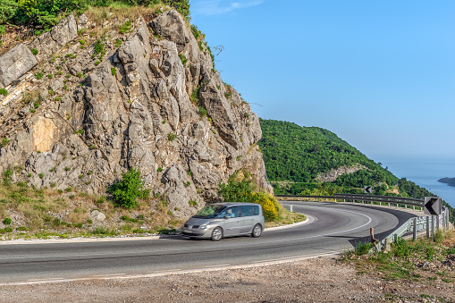 Blurred in fast motion car on mountain highway M2.3 near Budva, Montenegro. Traffic on a winding motorway among stone cliffs with a forest against the backdrop of the Adriatic Sea in the Balkans