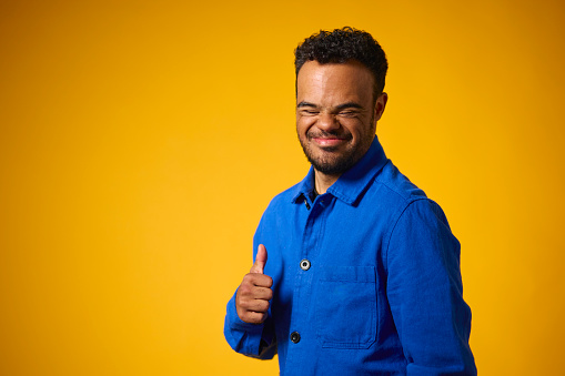 Studio Portrait Of Man With Down Syndrome Standing Against Yellow Background Giving Thumbs Up