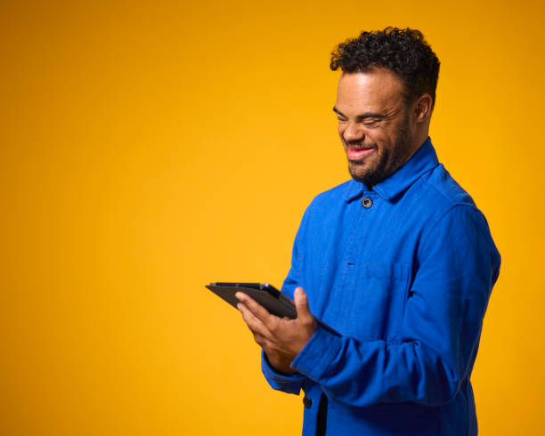 istock Studio Portrait Of Man With Down Syndrome Using Digital Tablet Against Yellow Background 1661155054
