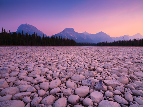Landscape during sunrise. Round rocks on the riverbank. Banff National Park, Alberta, Canada. Mountains and forest. Vivid colours during dawn. Natural landscape.