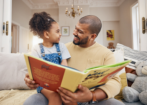 Man, child and book on sofa with smile, bonding and love in storytelling in living room together. Happiness, father and daughter reading story on couch for fantasy, learning and education in home fun