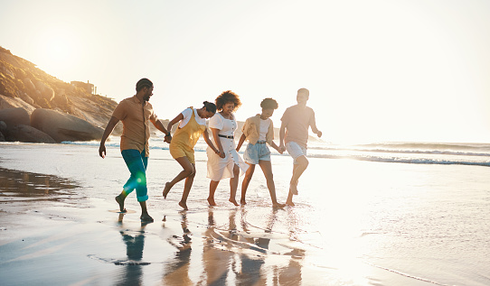 Summer, holding hands and sunset with friends at beach for freedom, support and travel. Wellness, energy and happy with group of people walking by the sea for peace, adventure and vacation together