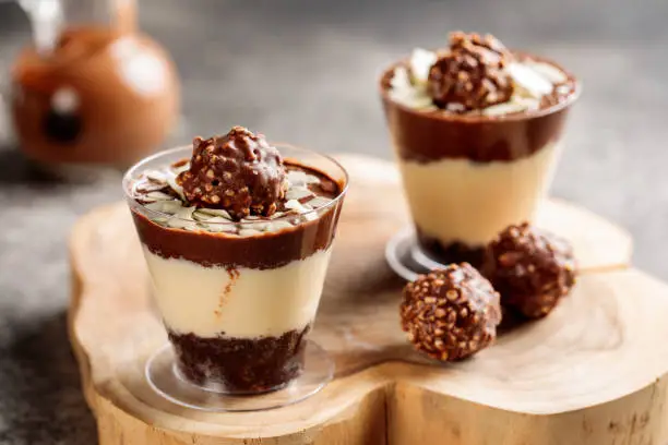 Photo of Ferrero rocher cheesecake served in cup isolated on wooden board top view cafe cheese cake food dessert