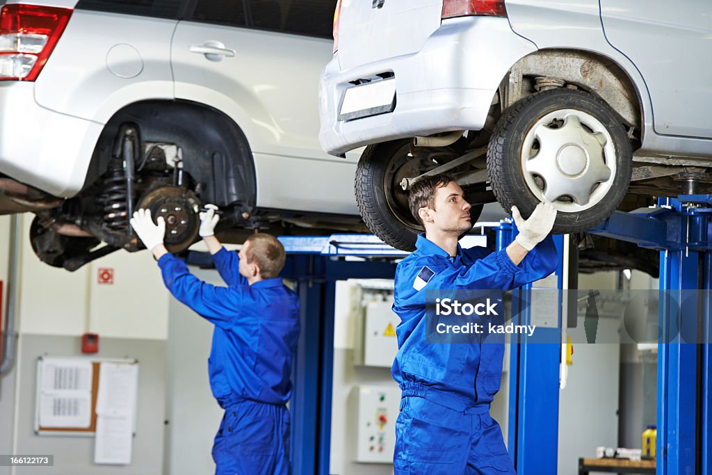Auto mechanics working on car suspension car mechanic inspecting car wheel and suspension detail of lifted automobile at repair service station Auto Repair Shop Stock Photo