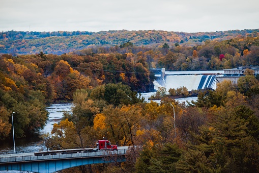 A truck traveling across a bridge with the Taylors Fall and autumnal forest in the background, Minnesota