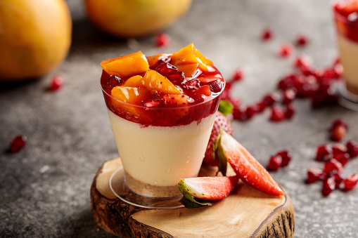 fruit cheesecake with strawberry, mango, pineapple and pomegranate seeds served in cup isolated on wooden board top view cafe cheese cake food dessert