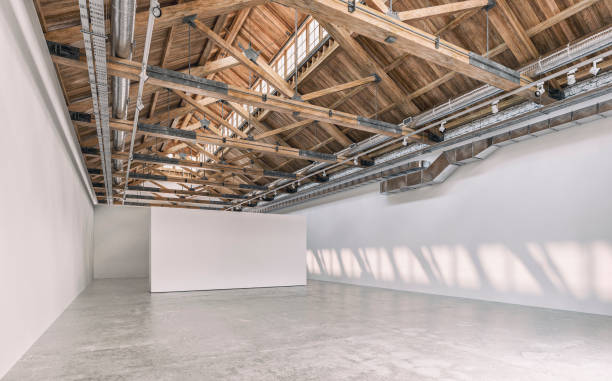 istock Side view of an empty white large gallery/showroom interior with white empty walls for events or artwork exposure, and a ceiling industrial construction with ventilation pipes, hardwood beams and reflectors (lighting equipment) 1661246120