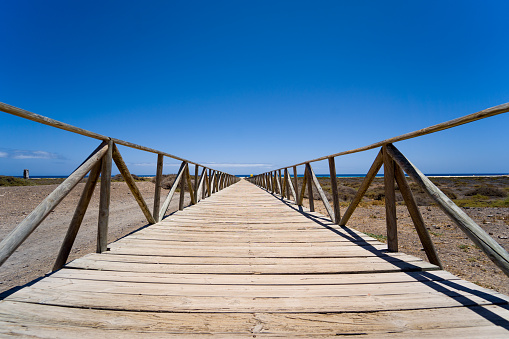 This photo captures the serene beauty of the wooden boardwalk pathway that guides visitors to Morro Jable Beach in Fuerteventura, Canary Islands, Spain. As you walk along this charming trail, you'll be surrounded by breathtaking coastal landscapes. With golden sands beneath your feet and the vast expanse of the Atlantic Ocean on the horizon, this pathway evokes a sense of exploration and discovery. Morro Jable Beach is a dream destination where each step brings you closer to the island's natural beauty and tranquility.