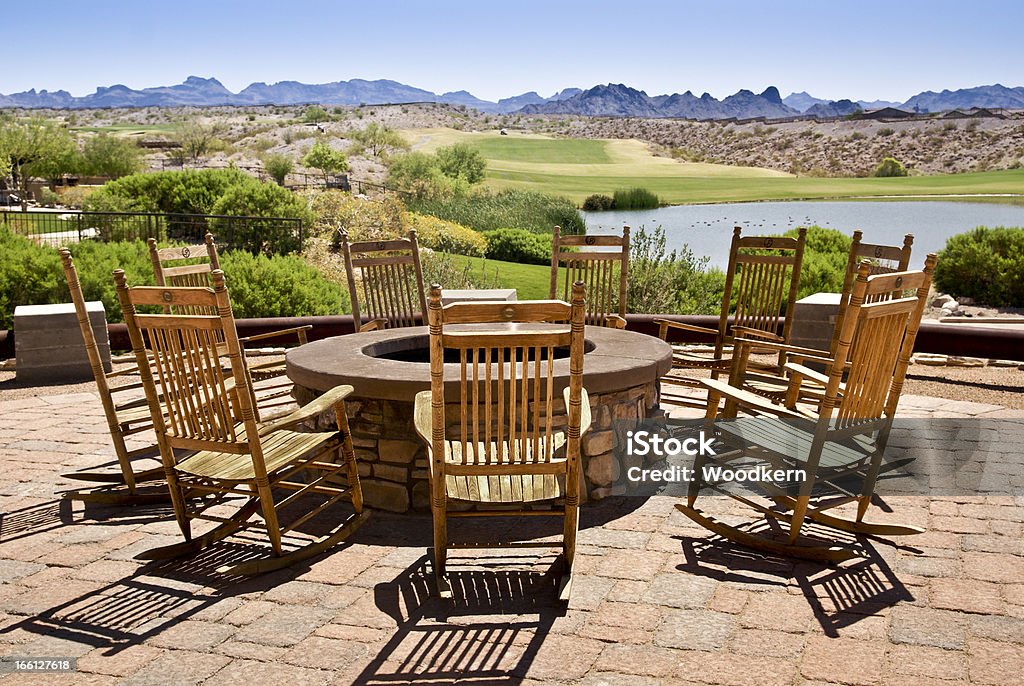 The 19th Hole Wooden rocking chairs, surrounding a firepit invite conversation beside a golf course and a pond. Fire Pit Stock Photo