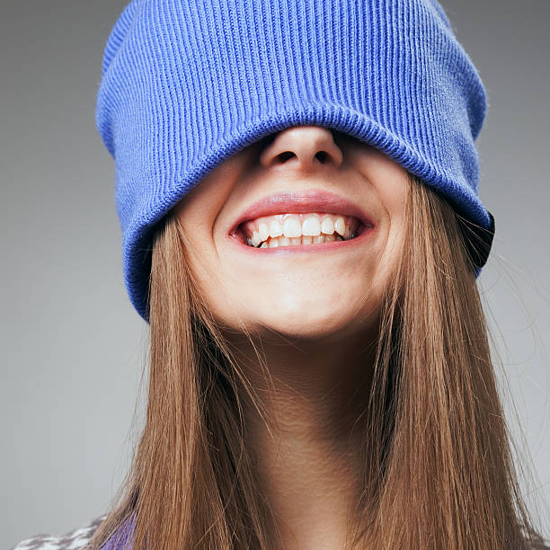 A cheerful woman wearing a yellow beanie and cozy sweater smiles warmly. The background suggests a city setting, adding a sense of urban vibrancy and joy to the scene.