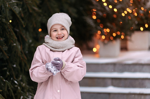 Girl in winter clothes on the background of Christmas trees and Garland lights. Girl on a decorated Christmas street. Banner on the theme of winter holidays with copy space.