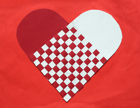 Heart shape woven of pieces of red and white paper, stuck on a red background of a brighter shade.