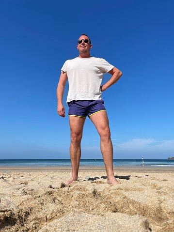 A sun tanned male in short shorts and white t-shirt enjoying the beach.