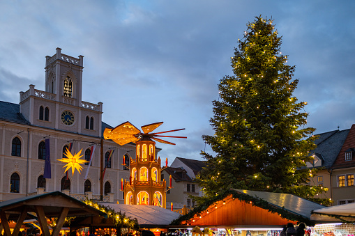 illuminated public christmas market with pyramid and decorated tree in front of town hall in weimar, germany