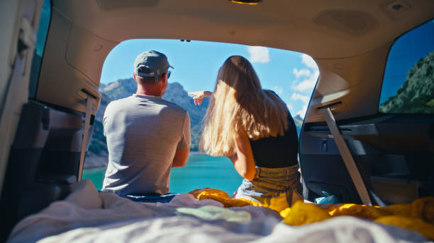 istock Loving couple resting and camping inside a large car trunk at lakeside. Drinking tea and looking at beautiful view celebrating 1661395403