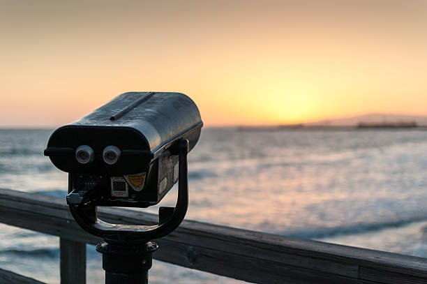 Coin-operated binoculars on pier at sunset overlooks ocean stock photo