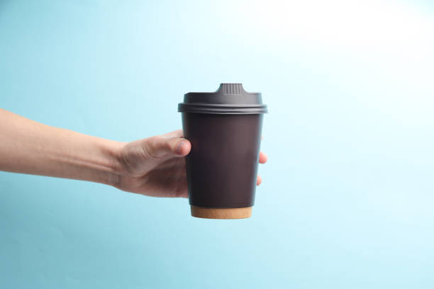 istock Hand holding brown Disposable take out cup for hot drinks (tea, coffee) on blue background 1661409323