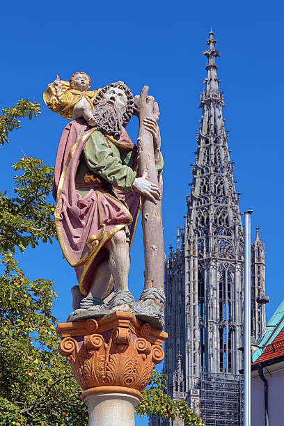 Statue of St. Christopher in Ulm, Germany Statue of St. Christopher carrying the Christ Child and Tower of the Ulm Minster, Ulm, Germany. Statue was erected in 1584. ulm minster stock pictures, royalty-free photos & images